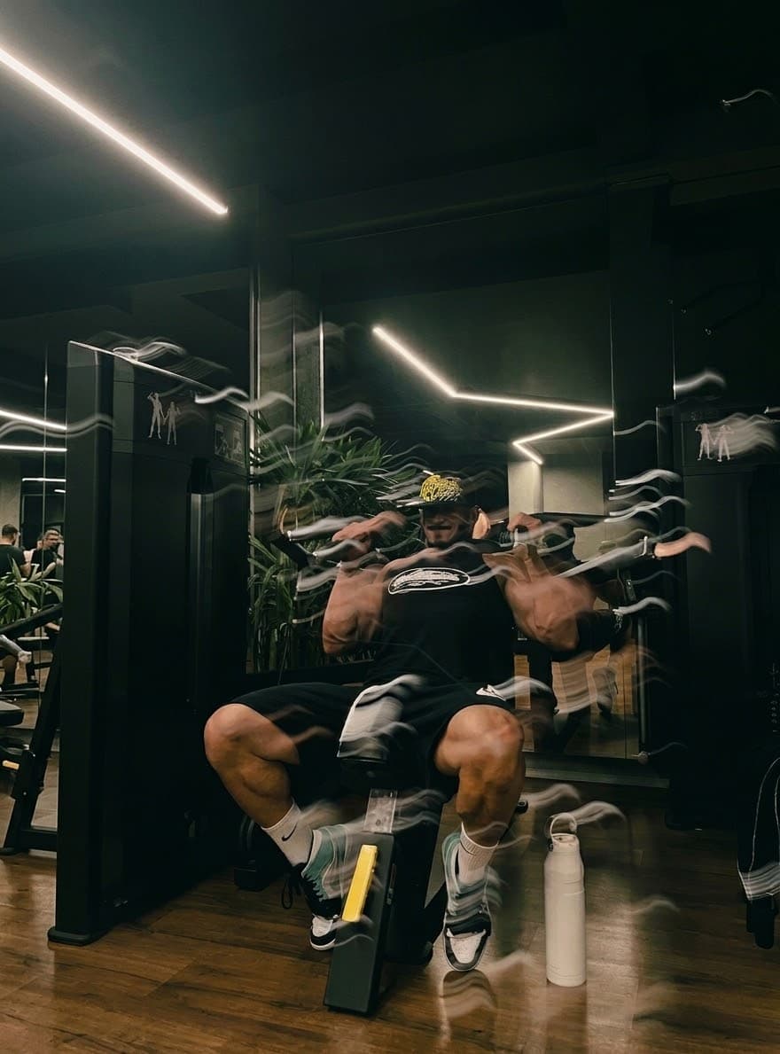 Alette otururken kollarını çift biceps pozuna kaldıran sporcu; elleri hareket bulanıklığında.